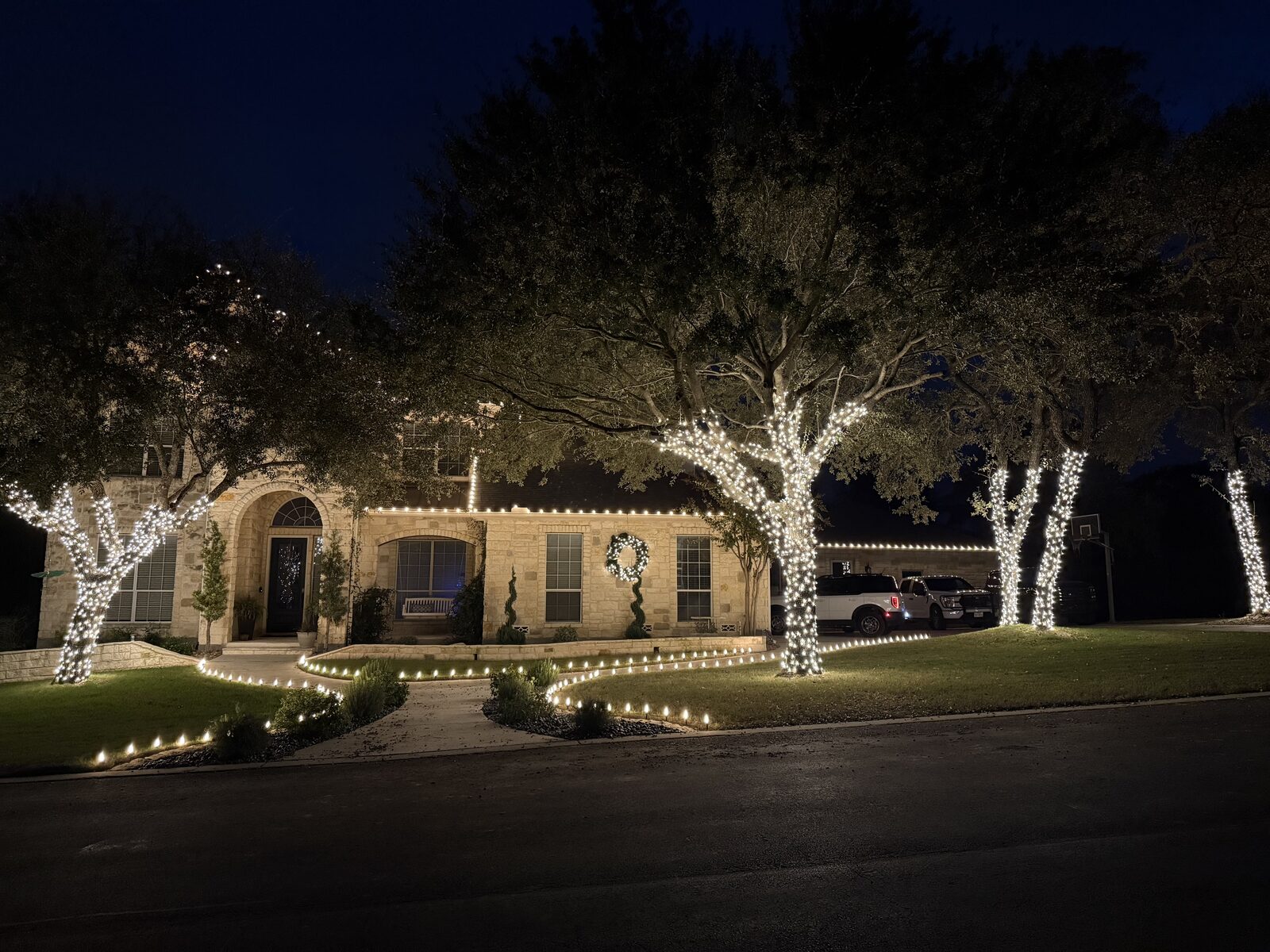 Stone home and trees lit with warm white Christmas lights at night