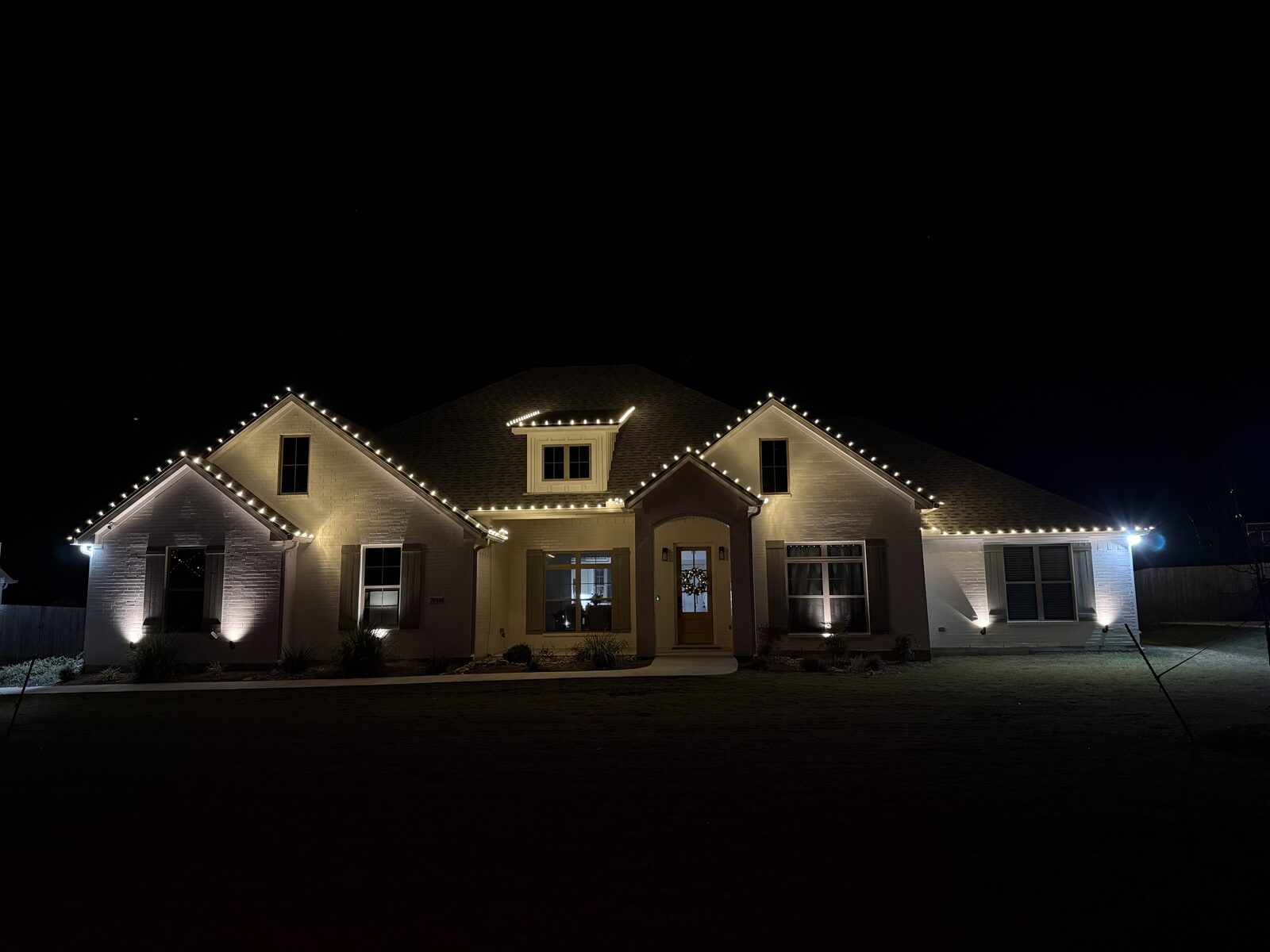 Brick home with clean warm-white Christmas lights along rooflines and gables
